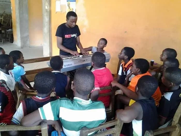 A volunteer plays while the class gathers round the keyboard · Accra