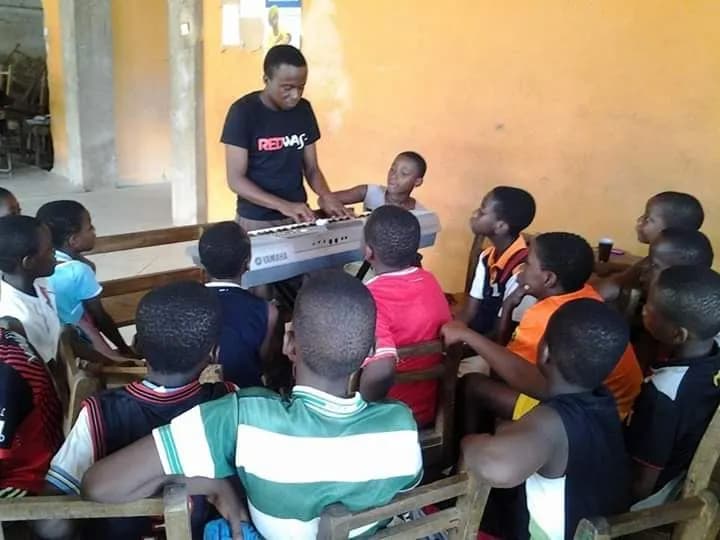 A volunteer plays while the class gathers round the keyboard · Accra